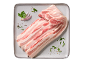 Felii de burtă de porc crudă cu pătrunjel și condimente pe o farfurie gri.
