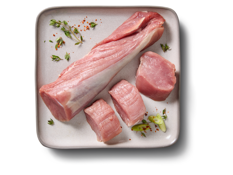 Mușchiuleț de porc crud întreg și tăiat cuburi, cu ierburi și condimente pe o tavă.