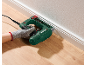 Capsator electric fixând o plintă albă pe un perete deasupra unei podele din lemn.
