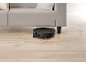 Aspirator robot negru curățând sub o canapea deschisă la culoare pe o podea de lemn.