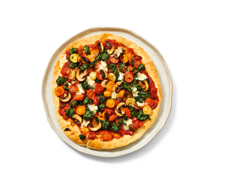 Pizza cu spanac, ciuperci, roșii cherry și brânză pe o farfurie albă.