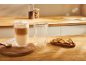 Latte macchiato într-un pahar cu perete dublu cu biscotti pe un blat de bucătărie din lemn.