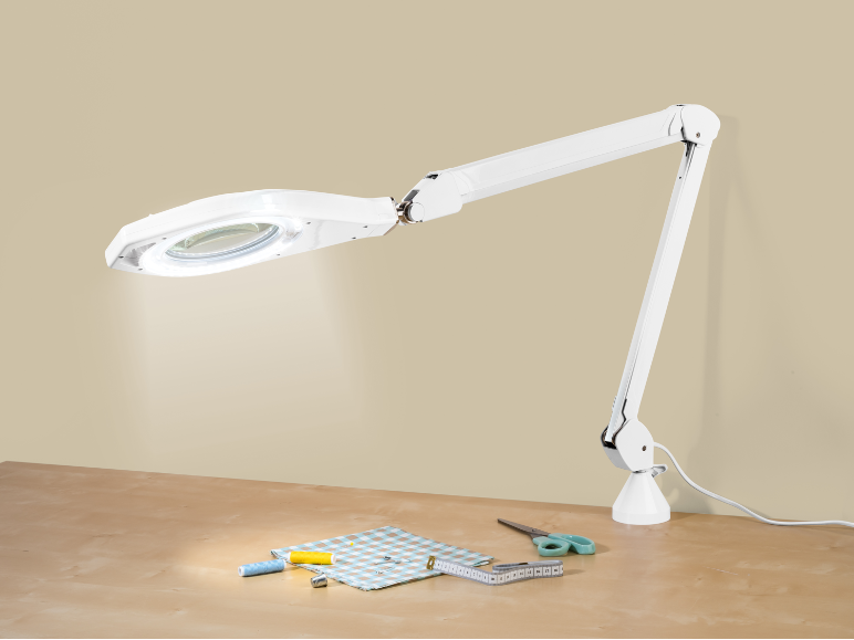 Lampă albă cu lupă LED deasupra unei mese cu materiale de cusut.