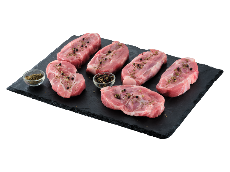 Fripturi crude de porc condimentate pe un tocător negru.