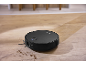 Aspirator robot negru curățând murdăria de pe o podea de lemn.