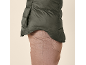 Prim-plan cu o persoană purtând o vestă matlasată verde închis peste pantaloni maro deschis.