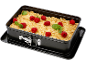 Prăjitură crumble cu zmeură într-o tavă dreptunghiulară cu pereți detașabili pe o tavă neagră.