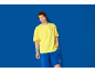 Bărbat în tricou galben și pantaloni scurți albaștri cu logo pe fundal albastru.