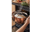 Bărbat punând o oală cu aburi în cuptor, cu legume proaspete și ierburi în apropiere.