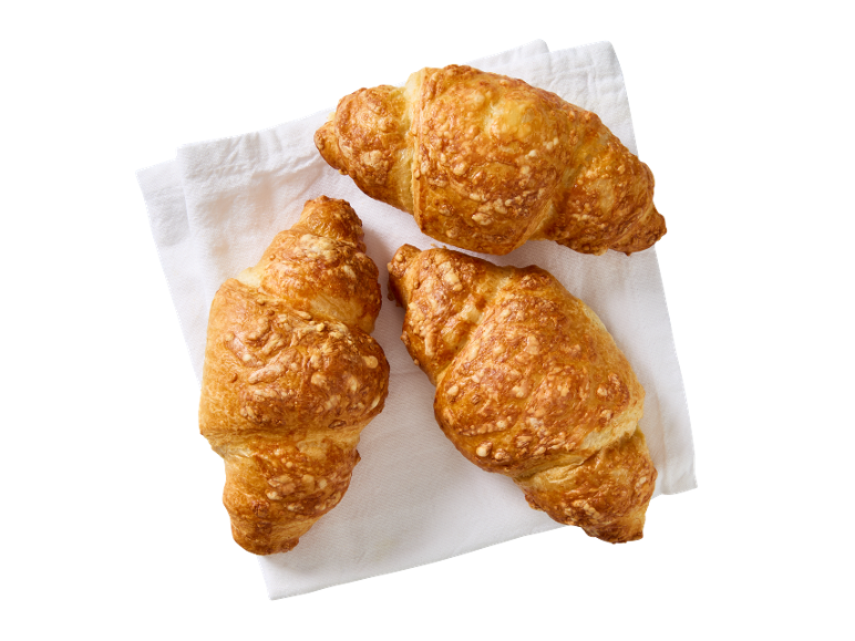 Trei croissante aurii cu brânză pe un șervet alb de pânză.