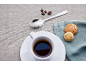 O ceașcă de cafea cu fursecuri, o lingură și boabe de cafea pe o masă.