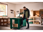 Bărbat în jachetă și pantaloni de lucru deschide o cutie de scule într-un atelier.
