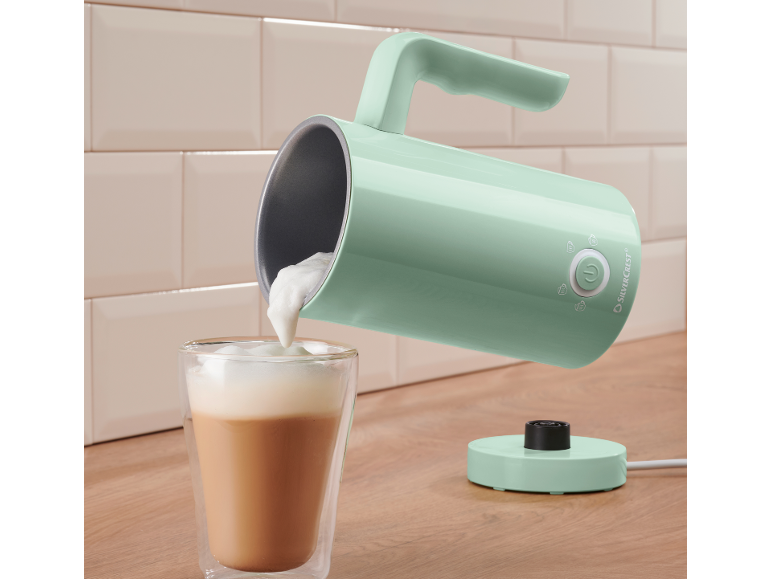 Spumator de lapte de culoare mentă turnând spumă într-un pahar de cafea.