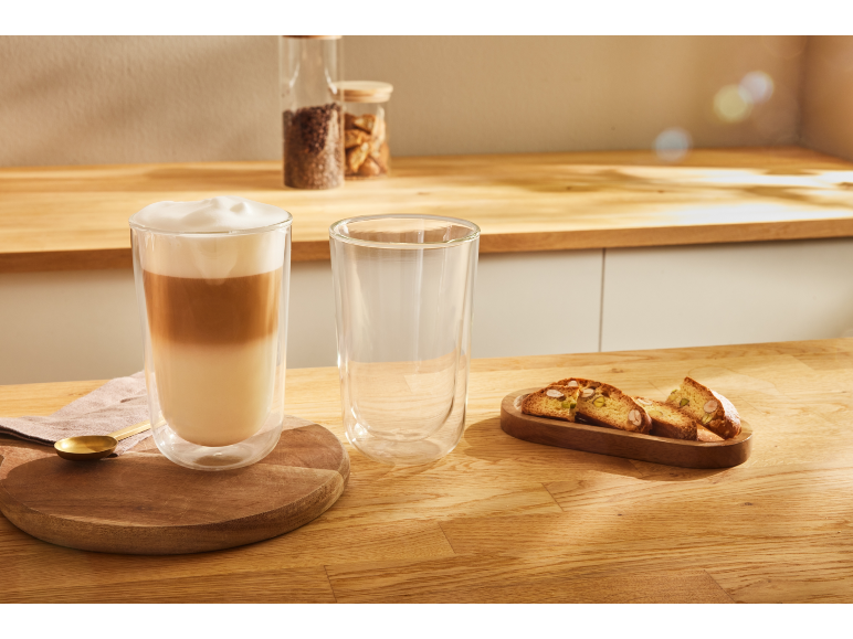 Latte macchiato într-un pahar cu perete dublu cu biscotti pe un blat de bucătărie din lemn.