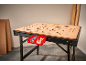 Un banc de lucru cu blat perforat din lemn, cu două recipiente roșii cu șuruburi și dibluri din lemn.