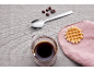 Cafea cu boabe de cafea, o lingură și o vafă pe un șervețel roz.
