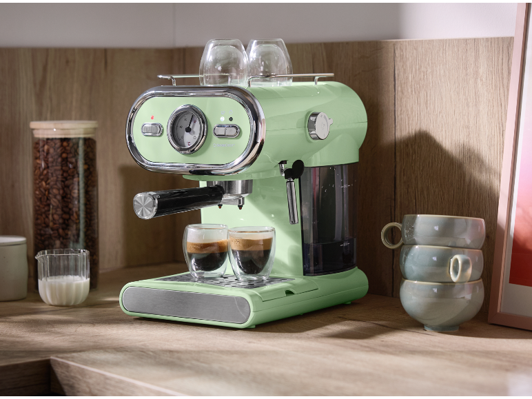 Espressor verde deschis cu două cești pe un blat de lemn.