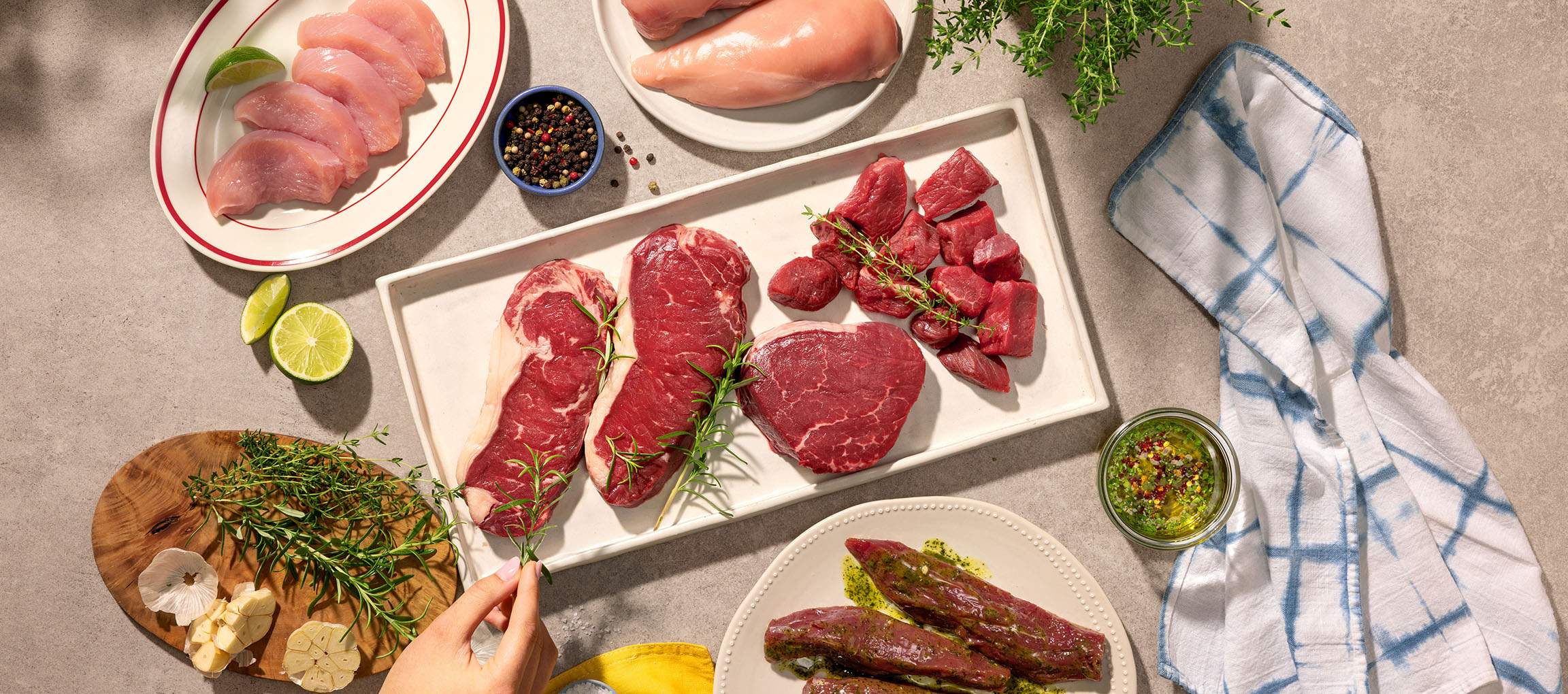 Diverse bucăți de carne crudă, inclusiv pui și vită, cu ierburi și condimente.