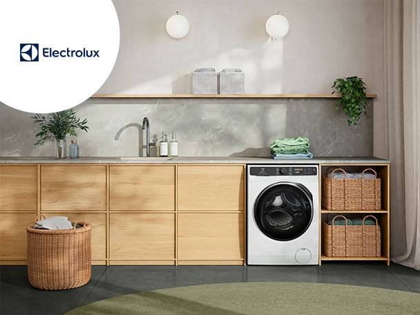 Mașină de spălat într-o spălătorie modernă cu chiuvetă, dulapuri din lemn și coșuri.