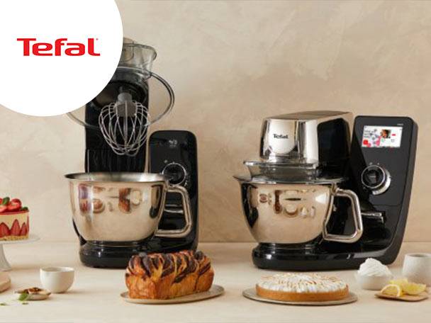 Două mixere de bucătărie negre și argintii, cu boluri metalice, înconjurate de prăjituri și produse de patiserie.