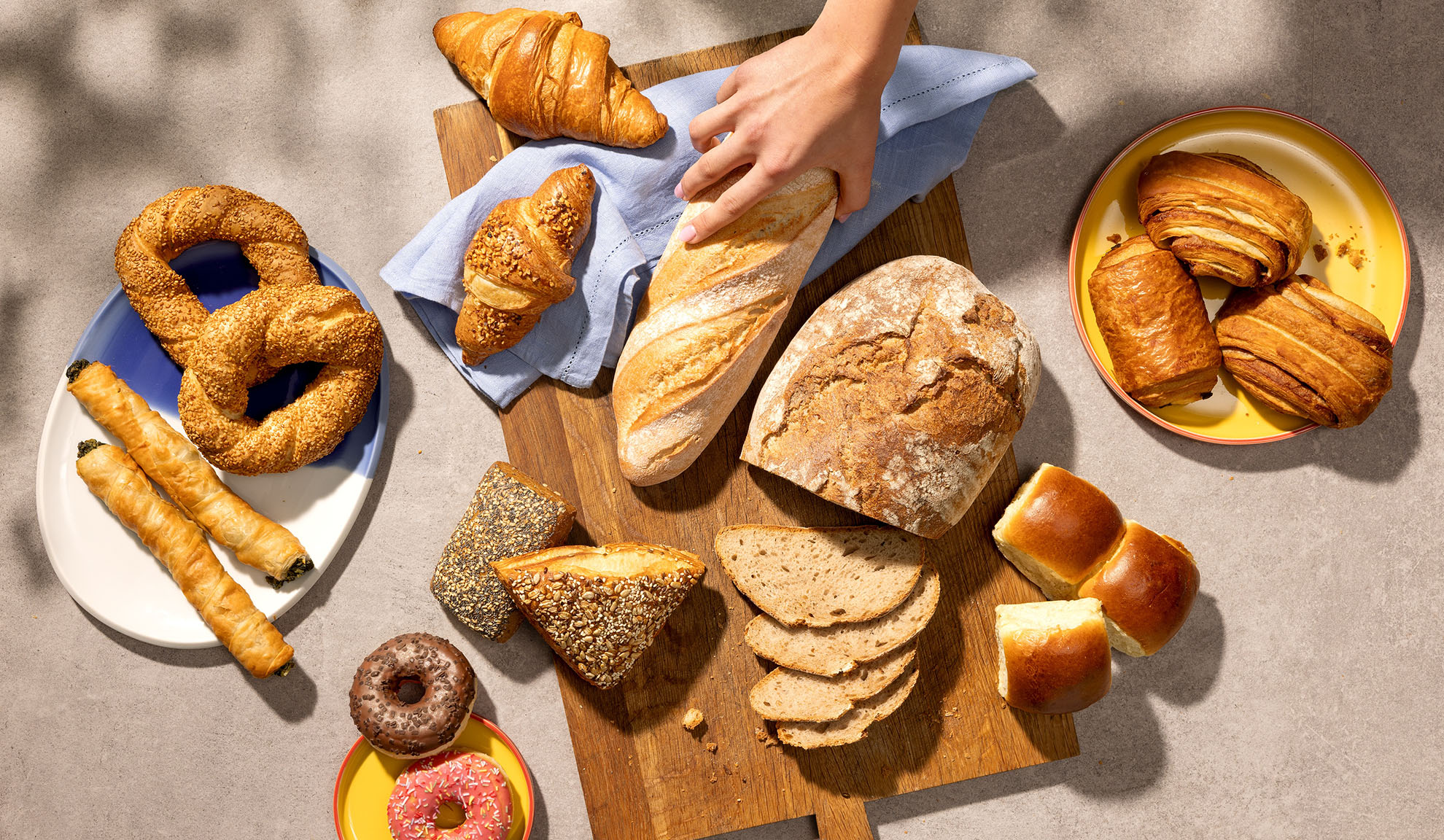 Asortiment de produse de patiserie proaspete, inclusiv pâine, croissante, produse de patiserie și gogoși pe o masă.