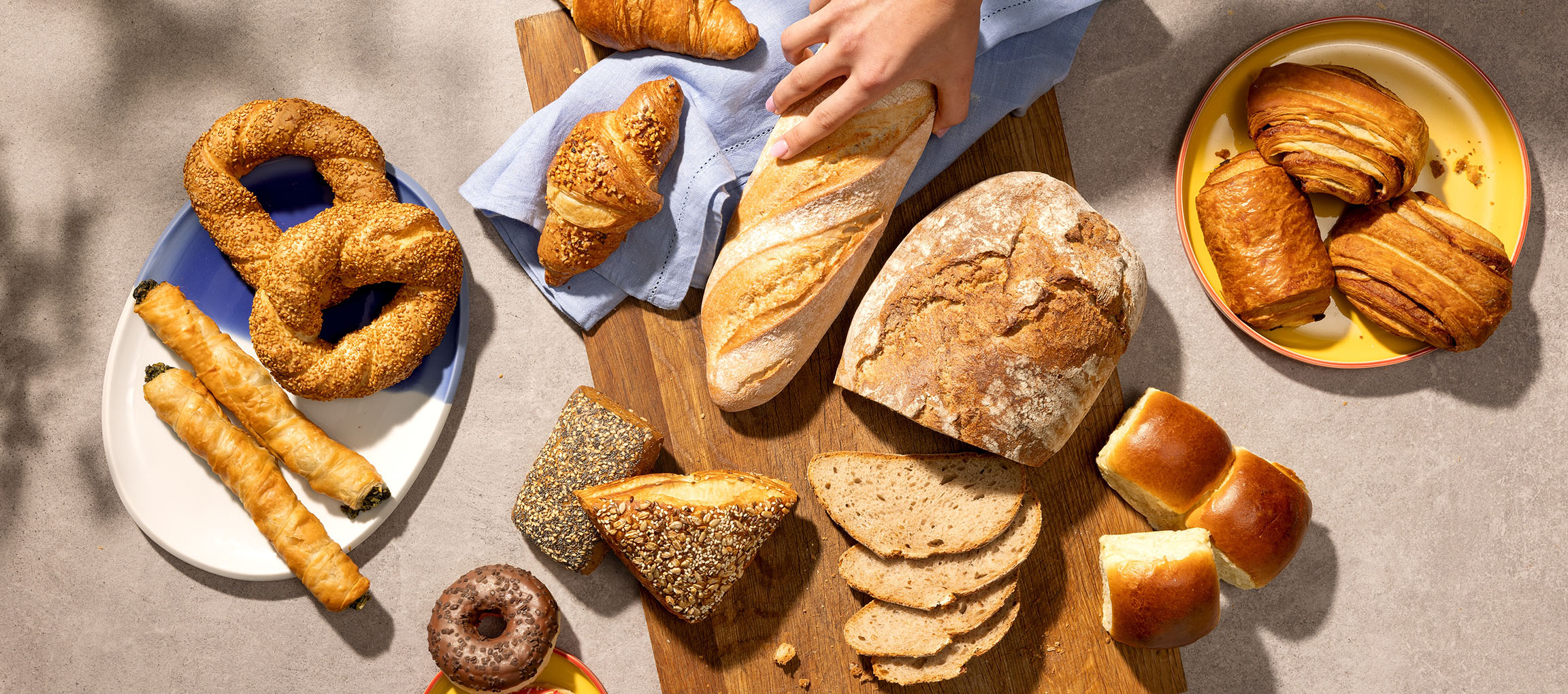 Asortiment de produse de patiserie și pâine, inclusiv covrigi, croissante și baghete, pe o masă.