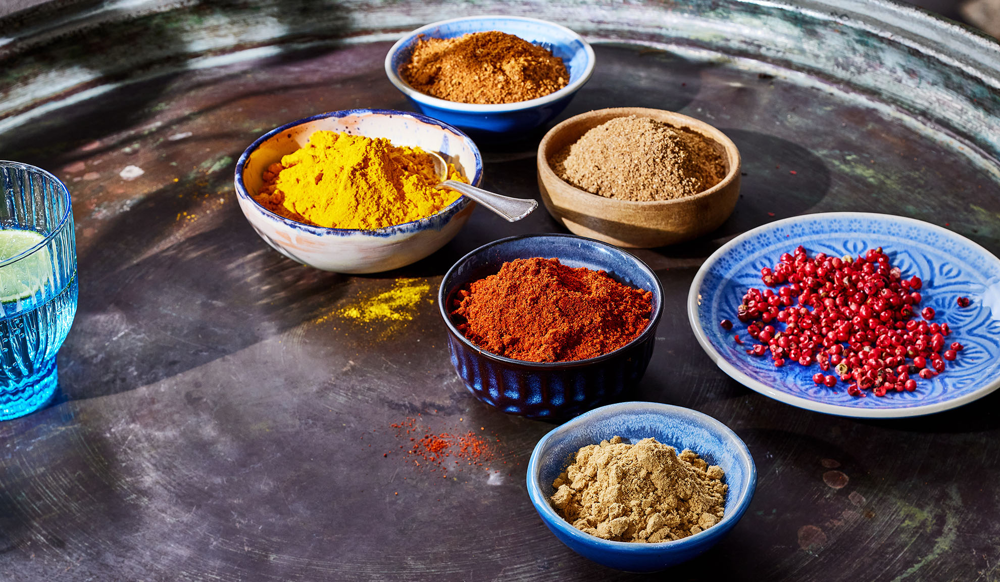Diverse condimente în boluri: turmeric, boia, piper și altele pe o tavă metalică.