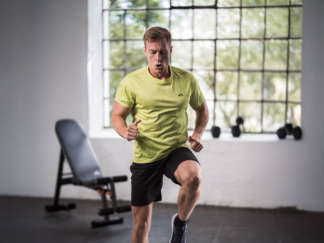 Bărbat în tricou galben și pantaloni scurți negri alergând într-o sală de sport.