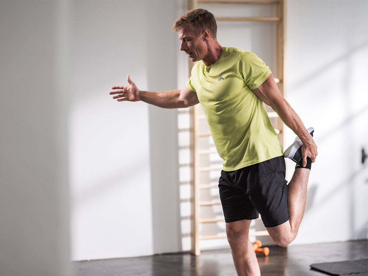 Bărbat care se întinde în pantaloni scurți negri și un tricou verde lime într-o sală de sport.