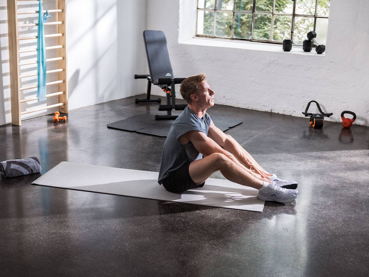 Un bărbat se întinde pe un covor de yoga într-o sală de sport cu echipament.