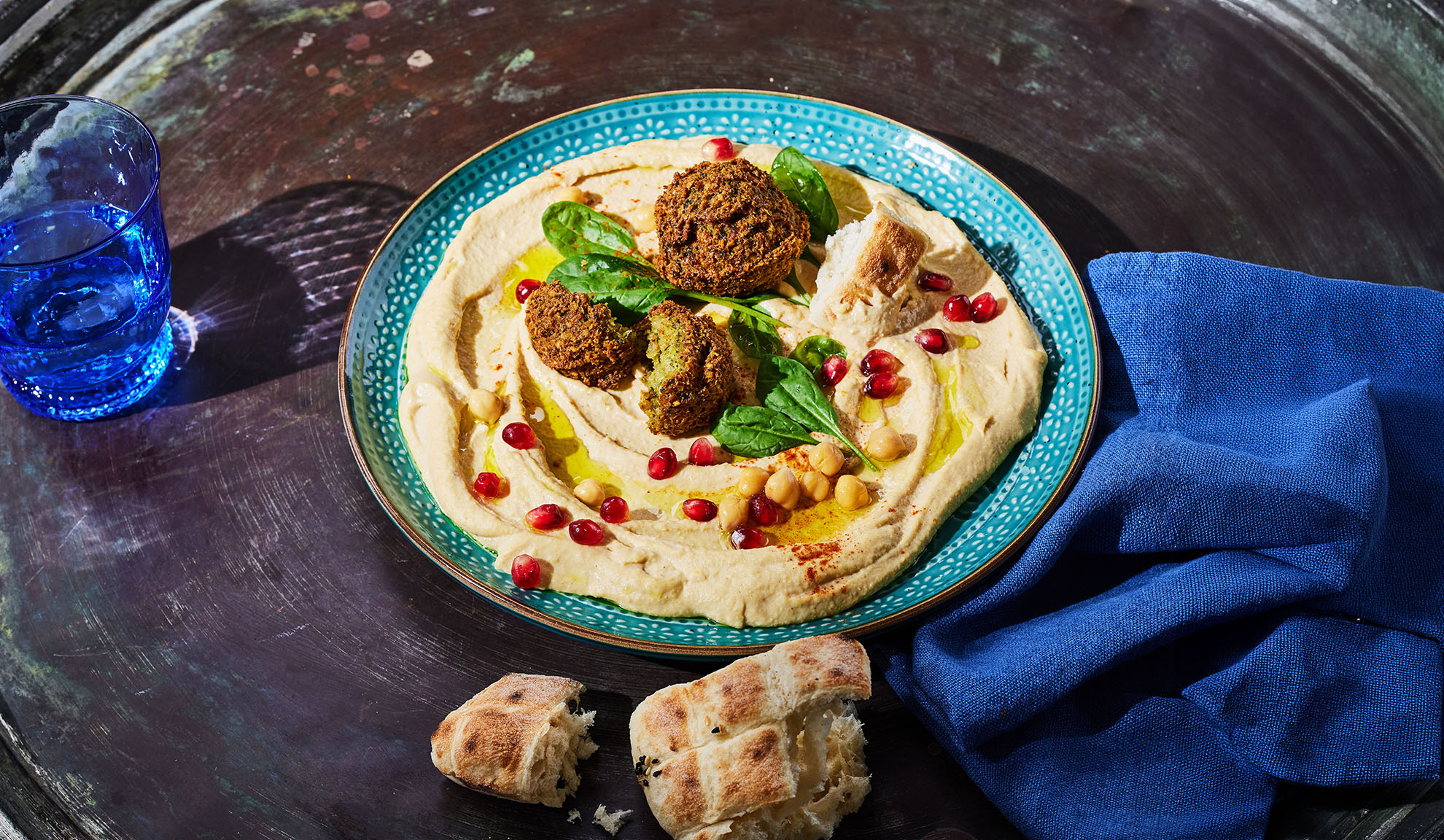 Humus cu falafel, semințe de rodie și pâine pita pe o masă întunecată.