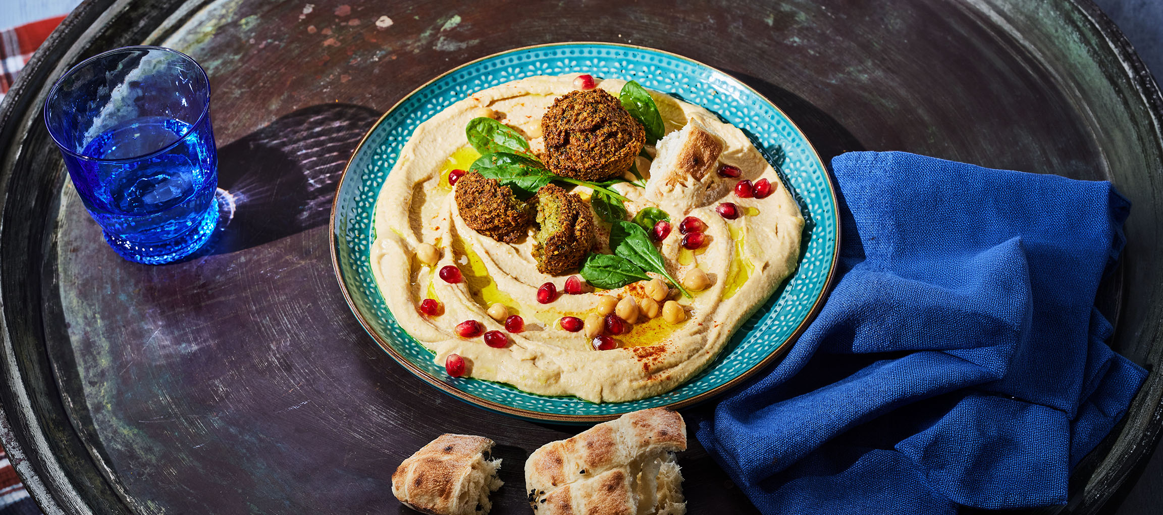 Humus cu falafel, semințe de rodie și pâine pe o tavă metalică.