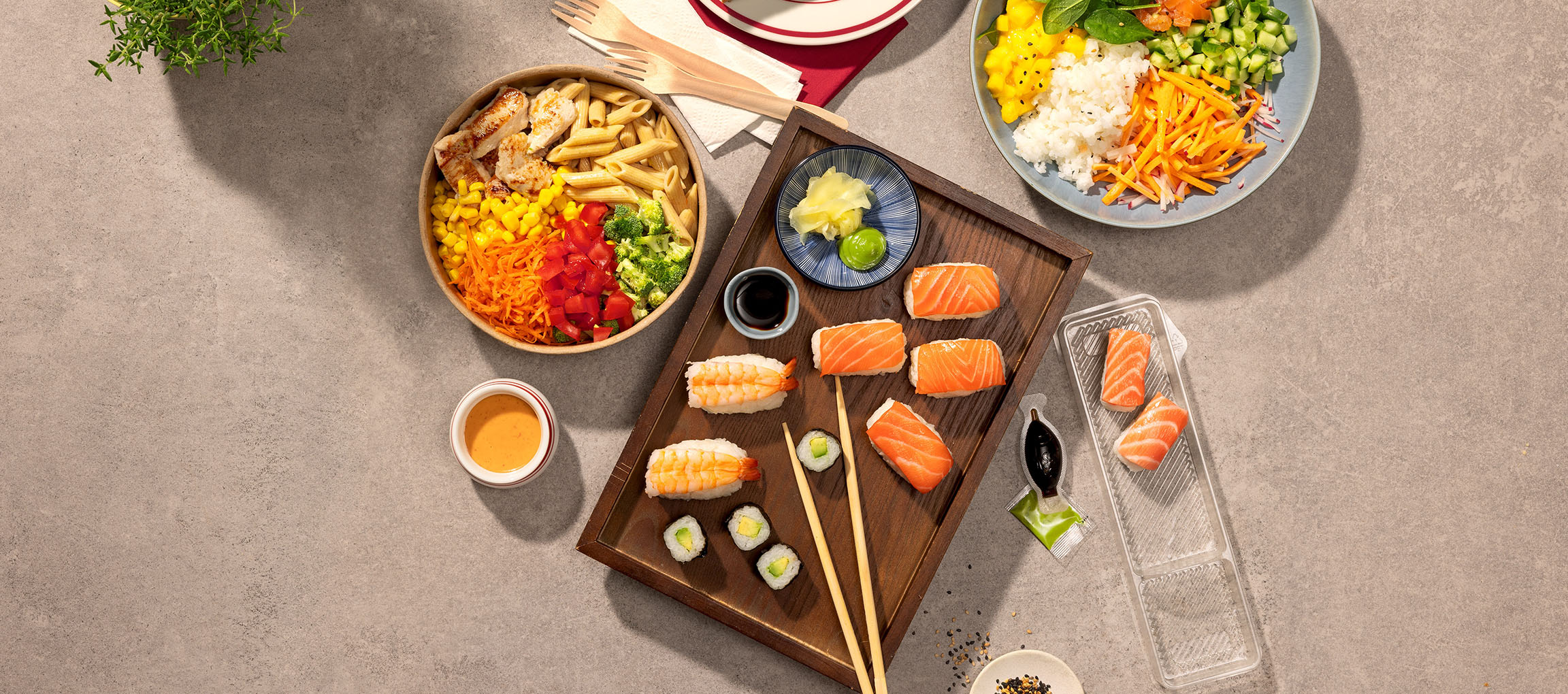 Mâncăruri asortate: bol cu paste și pui, sushi și un bol poke pe o masă.