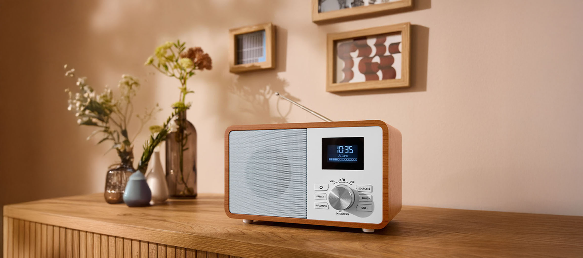 Un radio digital din lemn pe o comodă, cu vaze și tablouri pe perete.