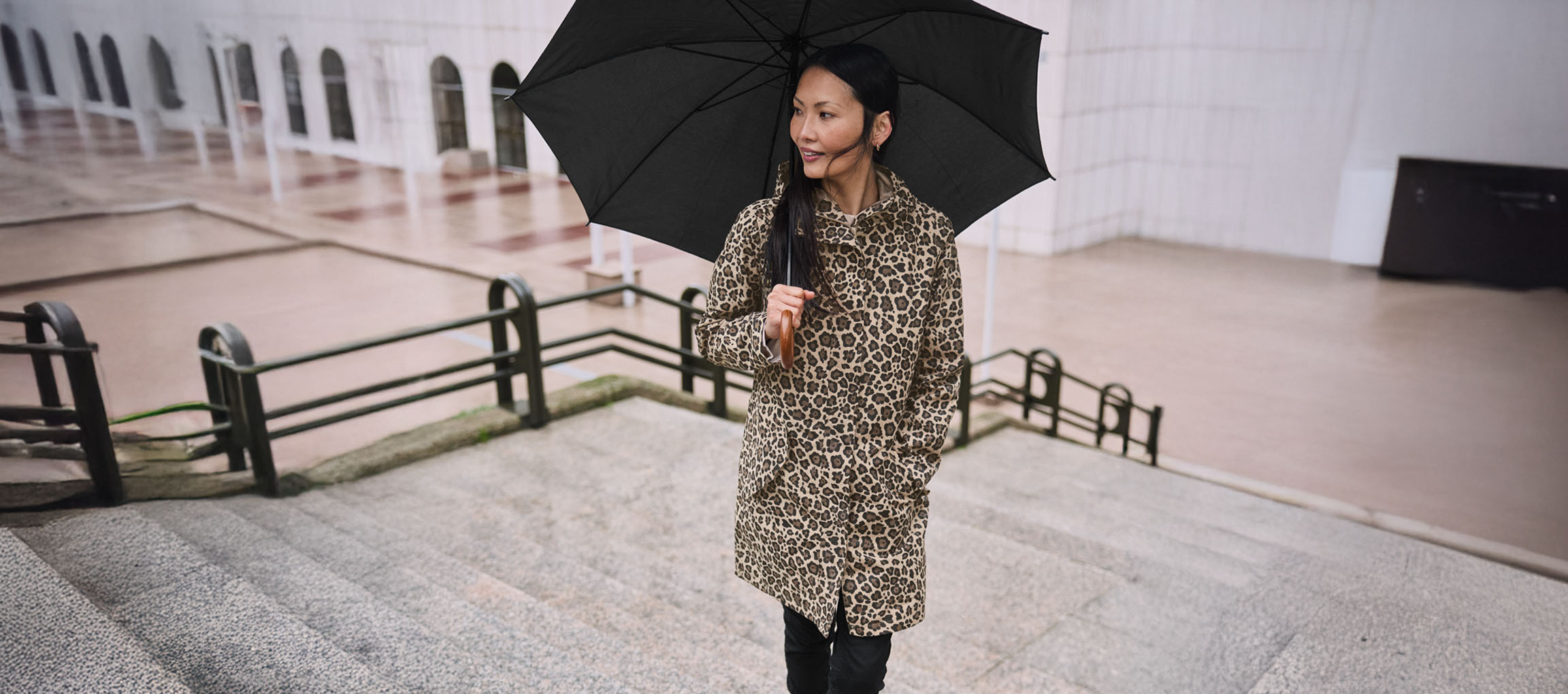 Femeie în palton leopard cu umbrelă pe scări.