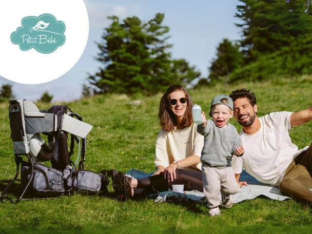 O familie fericită se bucură de un picnic în aer liber, cu un rucsac de transport pentru copii Petit Bébé.