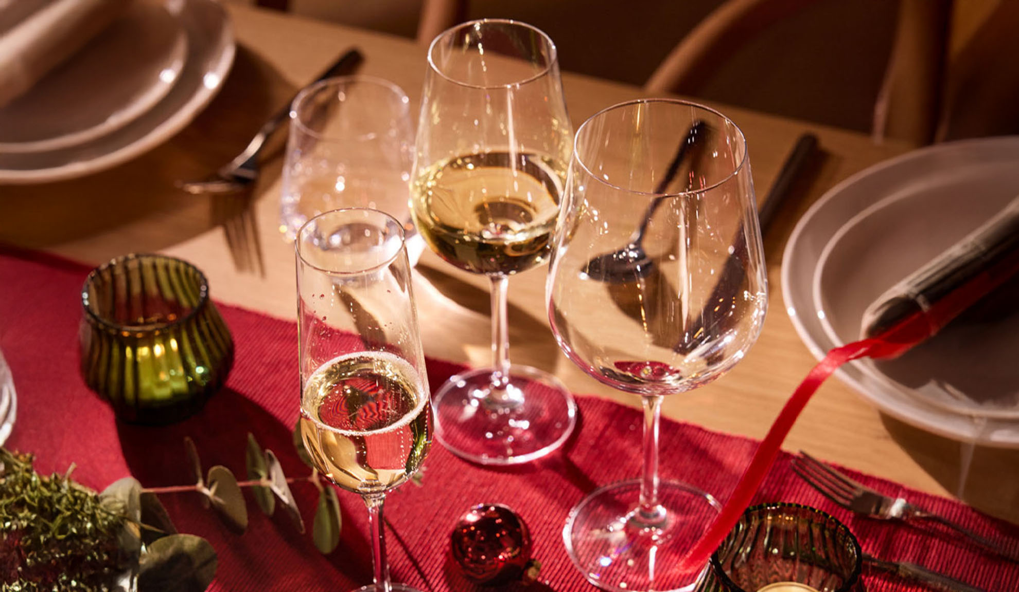 Masă festivă aranjată cu pahare de vin, pahar de șampanie și decorațiuni de Crăciun.