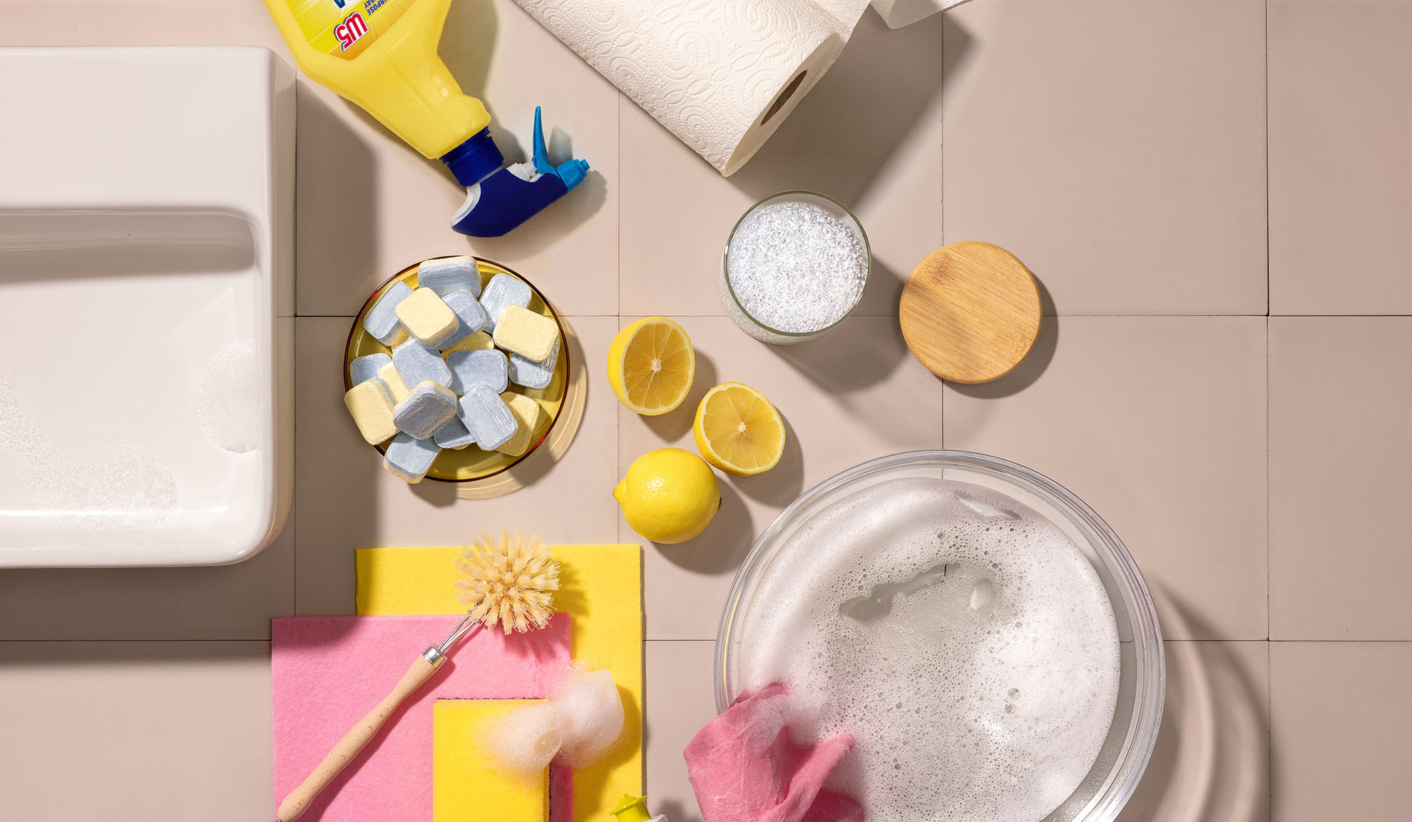 Produse de curățenie pentru casă, inclusiv detergent, bureți, lămâi și tablete pentru mașina de spălat vase.