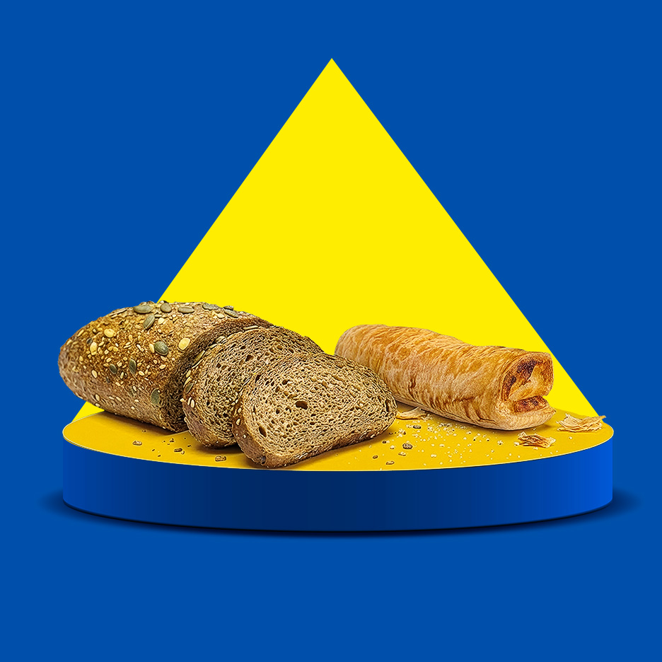 Pâine integrală feliată și un rulou de patiserie pe un piedestal galben și albastru.