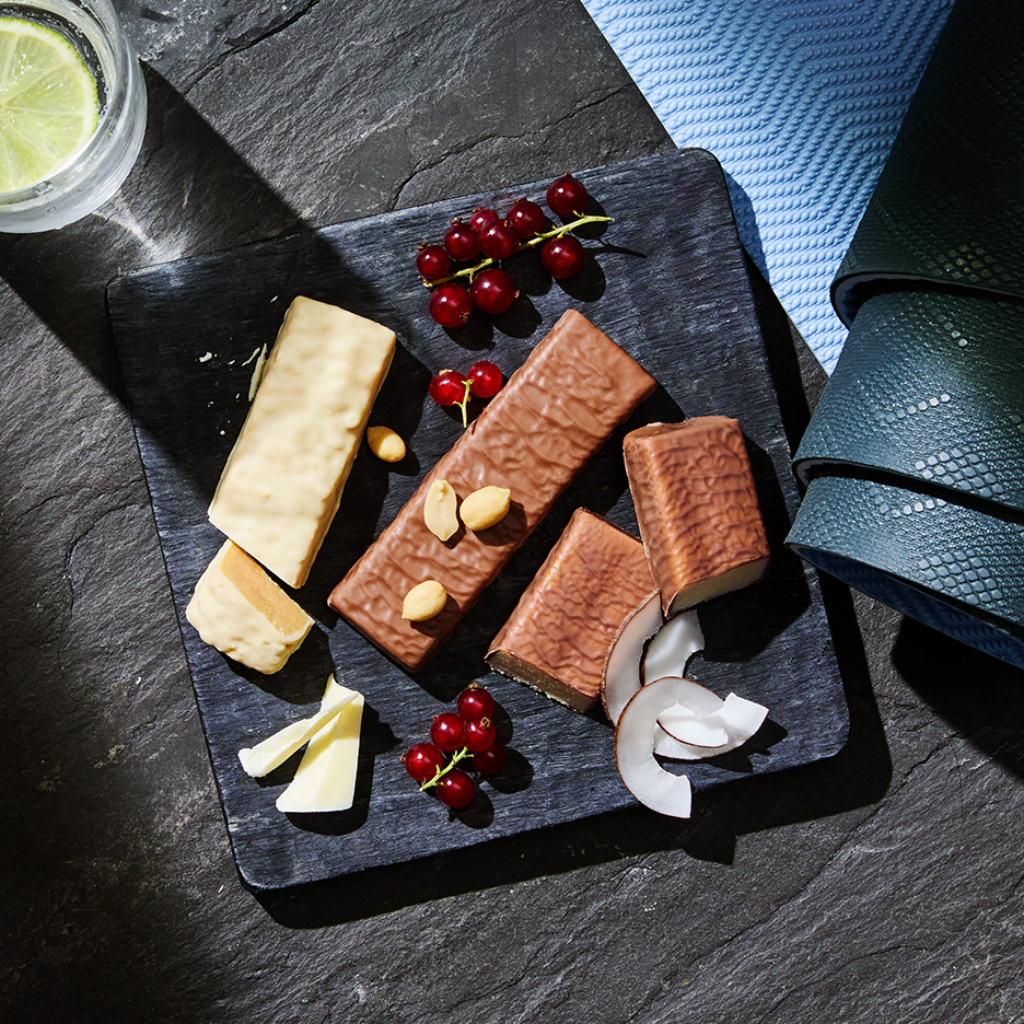 Batoane proteice, fructe de pădure și nuci pe o tavă de ardezie, cu o băutură răcoritoare și prosoape.