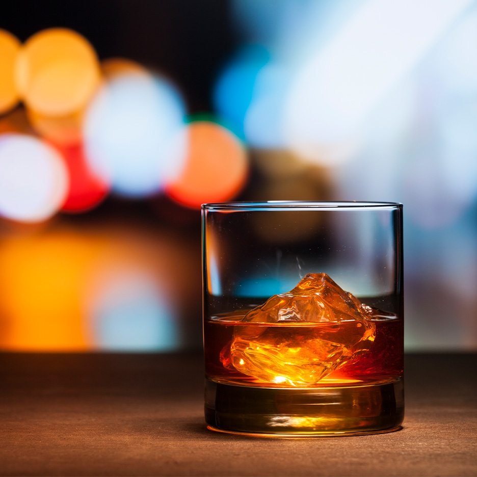 Pahar de whisky cu gheață, pe fundal bokeh colorat.