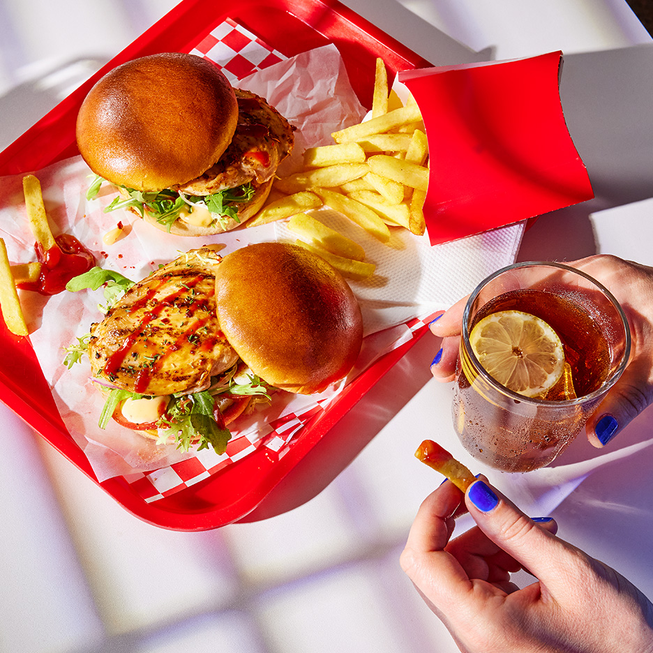 Doi burgeri de pui cu cartofi prăjiți și o băutură răcoritoare cu lămâie.