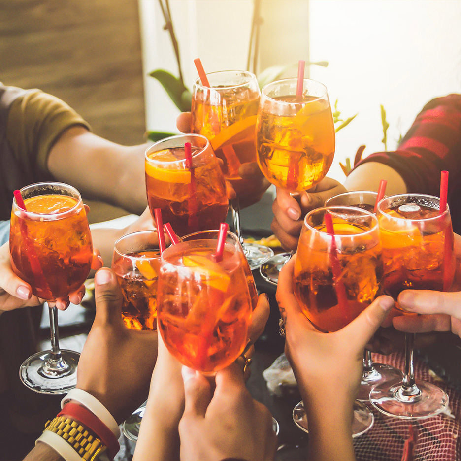 Grup de oameni ciocnind pahare cu cocktail Aperol Spritz.