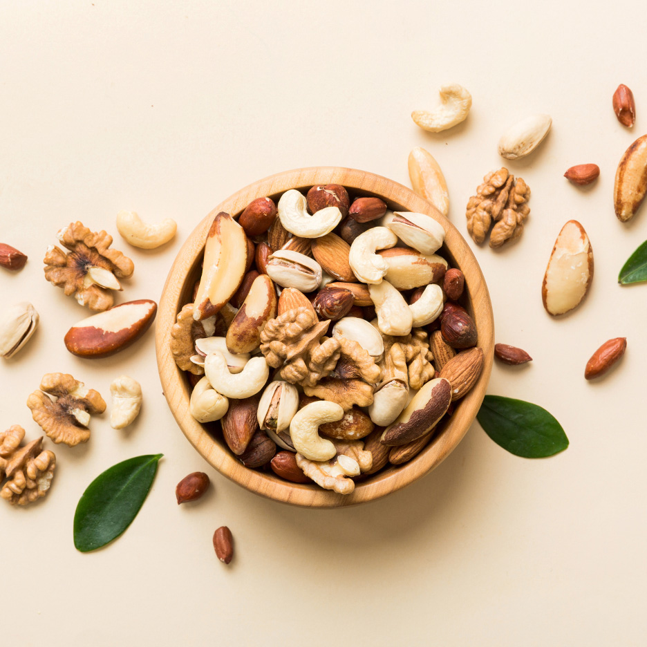 Un bol de lemn plin cu nuci asortate, inclusiv caju, nuci, migdale și fistic, pe un fundal deschis.