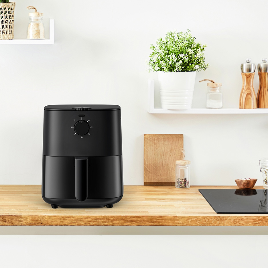 O friteuză cu aer cald neagră pe un blat de bucătărie din lemn, cu rafturi albe deasupra.