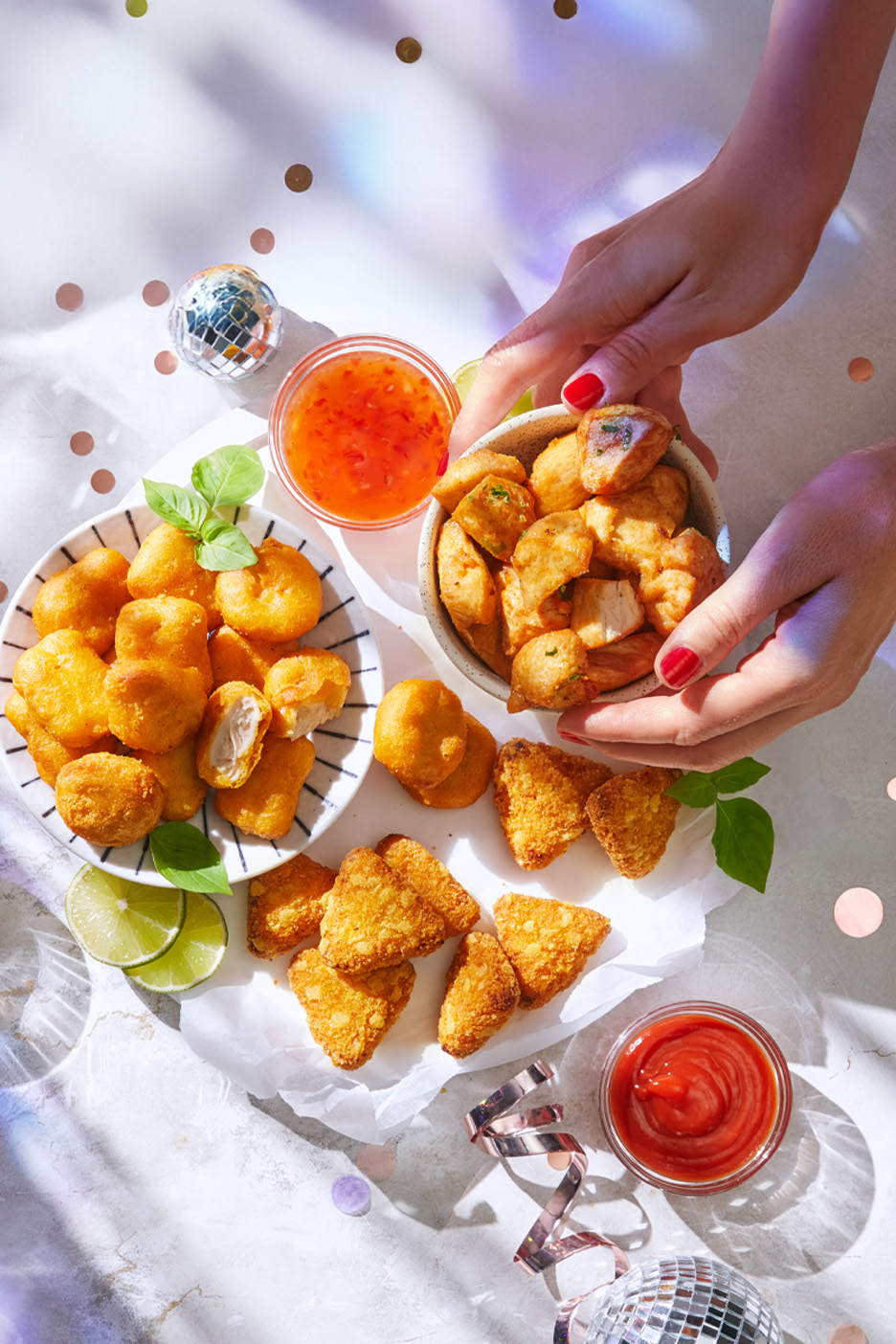 Diverse gustări prăjite, inclusiv nuggets și triunghiuri, cu sosuri și decor de petrecere.