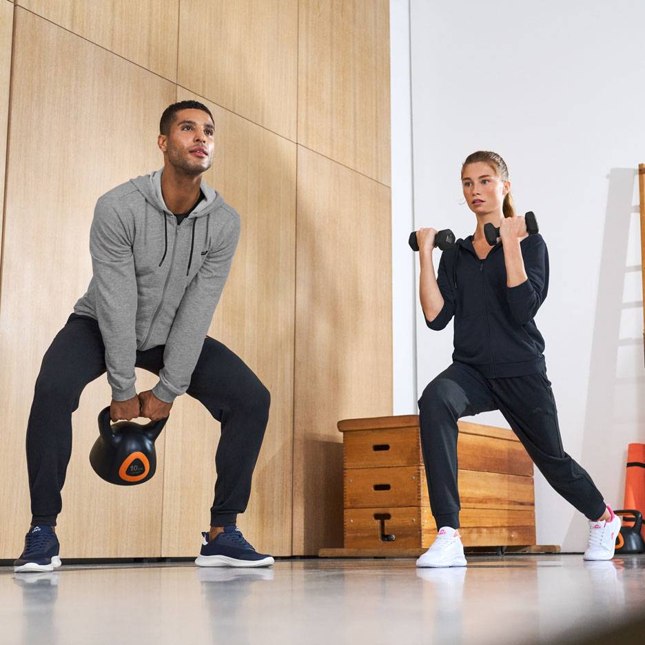 Bărbat și femeie în echipament sportiv, antrenându-se cu un kettlebell și gantere.