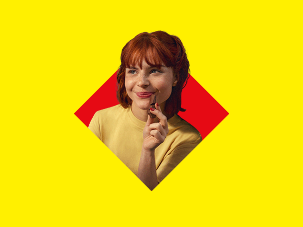 O femeie zâmbitoare cu păr roșcat, ținând o ciocolată, pe un fundal galben și roșu.