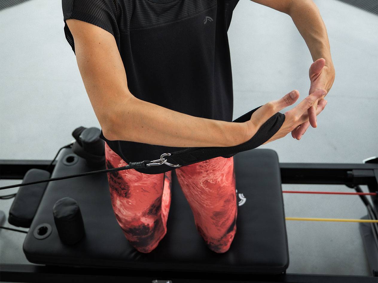 Femeie care face exerciții cu benzi de rezistență pe un aparat de Pilates.