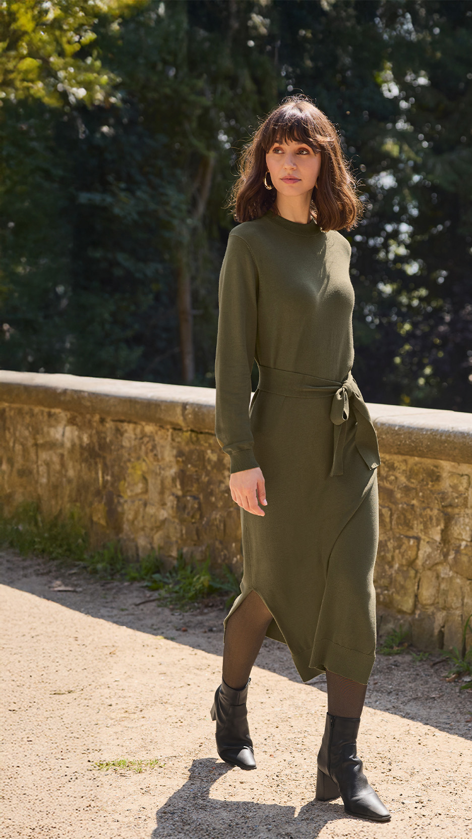 Femeie cu păr șaten, purtând o rochie verde măsliniu, cu mâneci lungi, în aer liber.